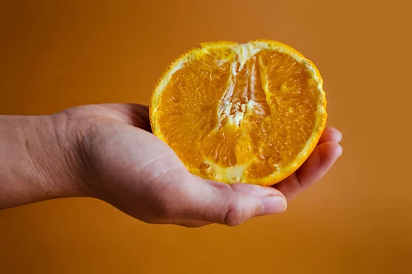 Tangan Wanita Memegang Setengah Oranye Pada Latar Belakang Oranye Kuning — Stok Foto