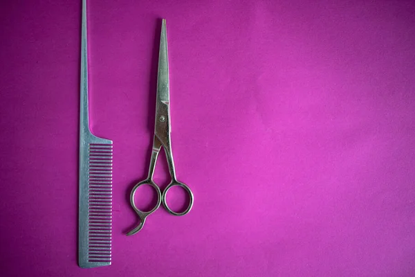 Stainless Steel Scissors And Comb On A Pink Background.