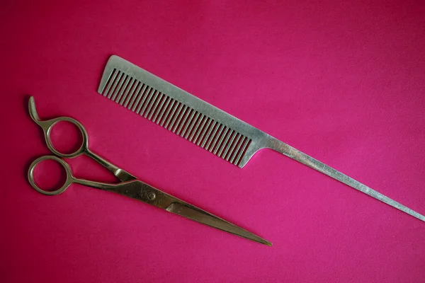 Stainless Steel Scissors And Comb On A Pink Background.