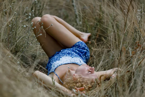 一个赤脚金发女人卷发坐在干枯的草场里 — 图库照片