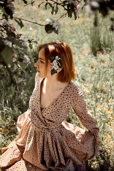 一位红头发的年轻白人妇女站在一棵开花的苹果树旁边 — 图库照片