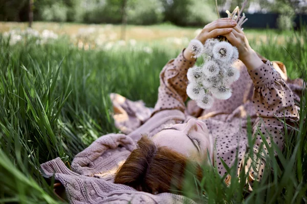 年轻美丽的女子手持蒲公英花束站在草地上 — 图库照片