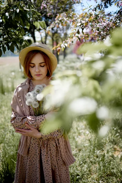 年轻美丽的女子手持蒲公英花束站在草地上 — 图库照片