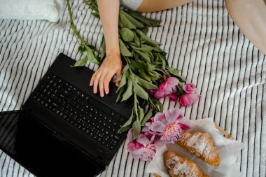 Güneşli bir sabahta yatakta elinde çay ve kruvasanla kadın bardağı tutuyor.