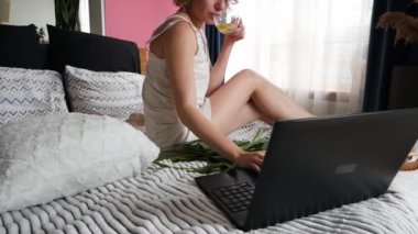 Yatakta ayçöreği ve kahve içerken dizüstü bilgisayar kullanan güzel bir kadın.