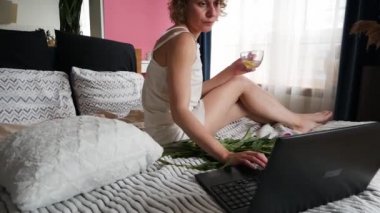 Yatakta ayçöreği ve kahve içerken dizüstü bilgisayar kullanan güzel bir kadın.
