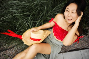 Çimenlerde uzanan Asyalı kadın kameraya bakıp mutlu bir şekilde gülümsüyor..