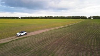İHA 'lar beyaz arabayı takip ediyor, boş yeşil alanda yolda ilerliyorlar.