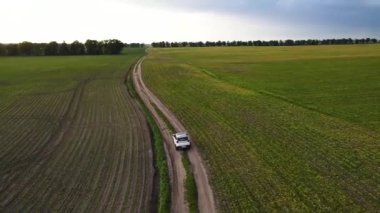 İHA 'lar beyaz arabayı takip ediyor, boş yeşil alanda yolda ilerliyorlar.