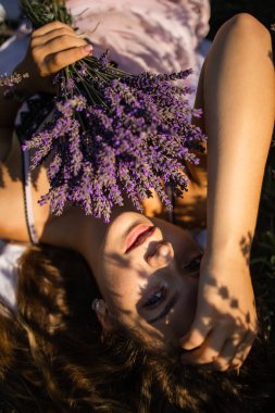 Şapkalı genç kadın yaz günü lavanta tarlasında yatıyor.