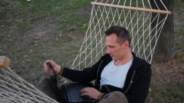 Genç İşadamı Park 'taki Bilgisayarda Hamakta Oturuyor.