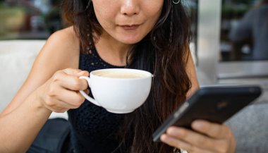Asyalı kadın kahve içiyor ve akıllı telefondan sohbet ediyor.