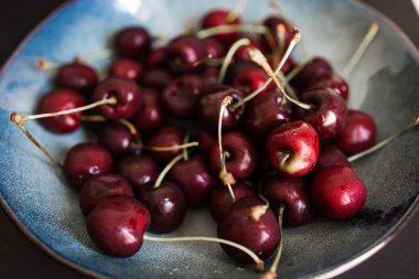 Mutfak masasındaki tabakta yakın plan kırmızı kirazlar.