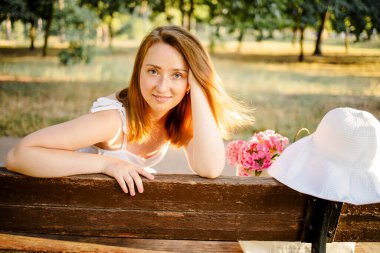 Mutlu kadın çimenlikteki bankta dinleniyor. Gülümseyen ve yukarı bakan genç sarışın kadının yüzünü kapat. Bir yaz gününde, rahat bir koltukta oturan bir kadın..