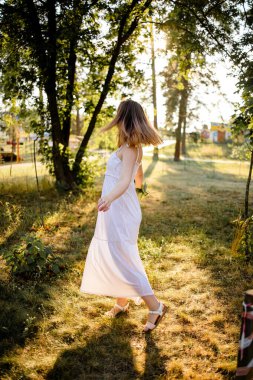 A Woman At The Park Wearing A Sweet Cute Dress Holding Flowers On A Warm Summer Day At Sunset.