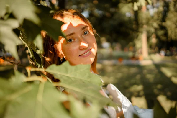 森林绿叶遮住脸的红头发年轻女子的特写 — 图库照片