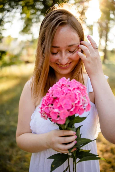 stock image A Woman At The Park Wearing A Sweet Cute Dress Holding Flowers On A Warm Summer Day At Sunset.