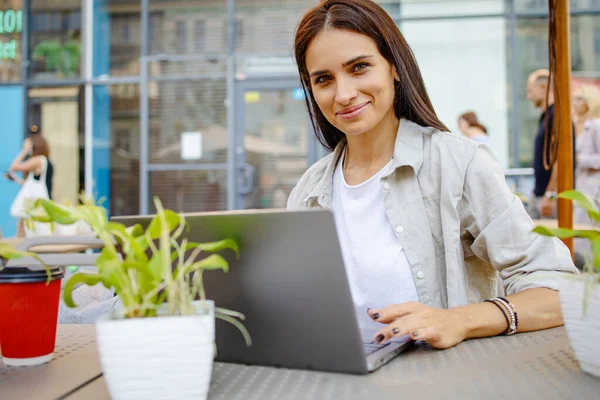 Güzel genç bir kadın laptopuyla dışarıda, kafede oturuyor.