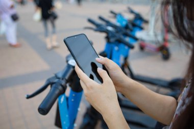 Bir kadının elleri modern şehrin elektrikli scooter 'ının yanında telefonu tutarak kilidi açacak. Modern şehir ulaşımı.