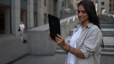 Tablet kullanan gülümseyen iş kadını. Şehir caddesinde yürürken müşteriyle video konferansı yapıyor..