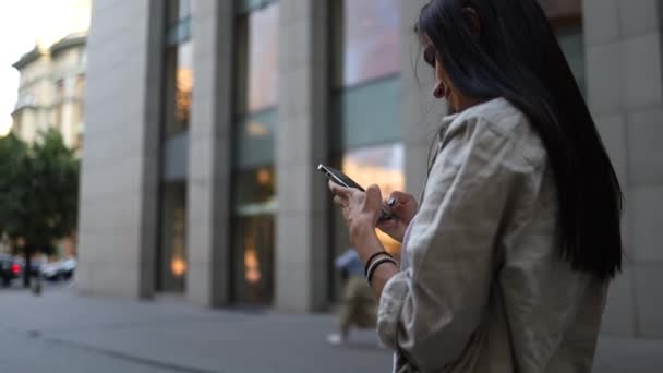 携帯電話の入力テキストメッセージを使用してシャツを着て笑顔の女性は ビジネス携帯電話の外にノートパソコンを保持歩くスマートフォンのスローモーション — ストック動画