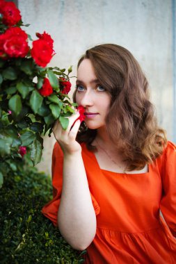 Bahar zamanı genç bir kadının portresi. Kırmızı güller çiçek açar. Gül bahçesinde kırmızı elbiseli bir kız..