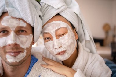 Karı koca kanepede uzanıyorlar ve maske portresini restore ediyorlar. Evde yardım kavramında sağlıklı yüz bakımı