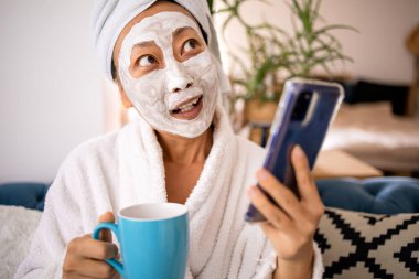 Asyalı kadının yüz maskesi takmasına ve cep telefonu kullanmasına şaşıran Happy, evdeki kanepede otururken iyi bir haber aldı. Güzel cilt bakımı ve sağlıklı sabah konsepti.