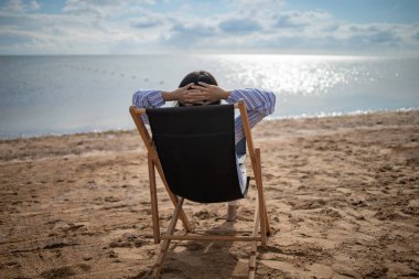 Yaz plajı tatili konsepti. Genç Asyalı kadın plaj sandalyesinde rahatla. Kopyalama alanı olan beyaz kum mavisi gökyüzü arkaplanı.