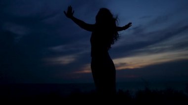 Kadın, Golden Hour Sunset View 'da gökyüzüne bakıyor. Güzel bir kadının silueti sabahları spor yapıyor ya da dışarıda yoga yapıyor. Spor sağlıklı yaşam tarzı kavramı
