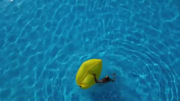 プールで黄色のインフレータブルでリラックスした若い筋肉マンのドローンオーバーヘッドワイドズームアウト — ストック動画