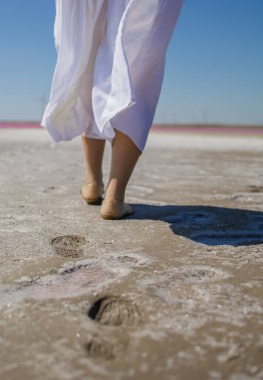 Beyaz uzun elbiseli güzel Asyalı kadın turist pembe tuz gölünde suda yürüyor.. 