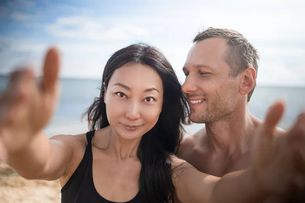 Couple relaxing on beach taking selfie picture with camera smartphone. Young multiracial couple on getaway vacation in Hawaii lying down looking at camera. Candid closeup angle looking candid real.