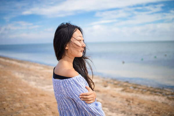 young asian girl is standing on the beach, looking away and thinking