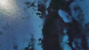 Turkuaz suda yüzen insanların insansız hava aracı görüntüleri. Adamın biri SUP tahtası ve kürek kullanıyor. Havadan üst görünüm