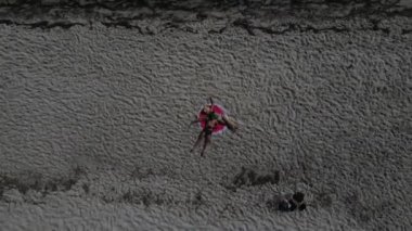 Yaz tatili - kumsalda güneş şapkası takan bir kız yukarıdan beyaz bir kum tepesinde. İnsansız hava aracının üst görüntüsü. Sıska bir kadının kumsalda güneşlenişini gösteren hava manzarası. .