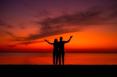 Romantik aşıkların silueti arka planda renkli günbatımında sarılıp öpüşüyor. Aşk konsepti.