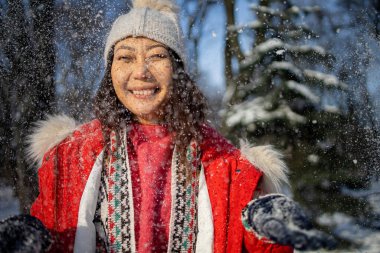 Kış ormanında kar yağmasını bekleyen gülümseyen Asyalı genç bir kadının portresi.