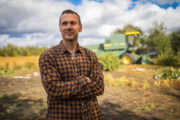 Portrait of a handsome young farmer standing in a shirt and smiling at the camera, on a tractor and nature background. Concept: bioecology, clean environment, beautiful and healthy people, farmers.