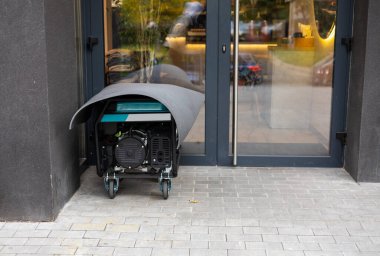 Electric generator stands on a street and supplies electricity to a shop or cafe during blackout. Concept of backup power supply and blackout