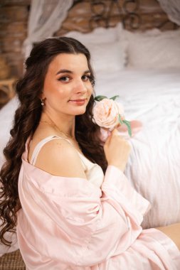 Güzel bir gelin zarif bir şekilde güneş ışığında poz verir, ince bir dantel bornoz giyer. Işık, onun sakin ifadesini ve gelinlik giysisinin karmaşık detaylarını vurguluyor.