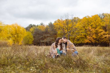 Sonbahar parkında çimlerde oturan ekoseli genç bir çift.
