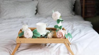 Ev ışığı modern bir iç mekanda pembe çiçek demeti. Sabahları yatak odasında taze çiçekler. Yataktaki masada bir fincan kahve ve beyaz çiçekler..