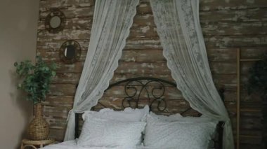 Şık bir yatak odası, beyaz çarşaflar ve yumuşak yastıklarla süslenmiş rahat bir yatak içeriyor. Boho şık tasarımını geliştiren bitkilerle huzurlu bir atmosfer yaratıyor..