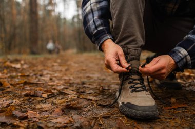 Sonbahar ormanında yürüyüş ayakkabısına ayakkabı bağı bağlayan bir adam. Turist, Woodland Trakking Patikası 'nda sonbahar yürüyüşüne hazırlanıyor. Etkin yaşam biçimi 