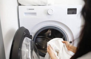 Ev hanımı çamaşır makinesi kullanıyor, çamaşırları makineye yüklüyor..