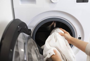 Ev hanımı çamaşır makinesi kullanıyor, çamaşırları makineye yüklüyor..