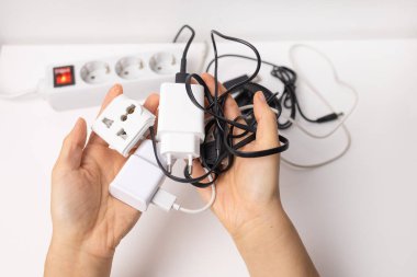 Beyaz uzatma kablosunun yanında çeşitli elektrikli aletleri tutan eller. Elektrik aşırı yüklenmesi. Aşırı yüklenmiş güç prizleri, kapat