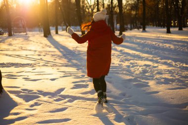 Tanımlanamayan, sıcak kıyafetli, karlı çayırların arasında tek başına duran ve kış ormanlarında gün batımını hayranlıkla izleyen bir kadının arka görüntüsü..