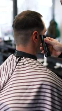 Genç bir erkek berber erkek bir müşterinin saçını düzeltir. Profesyonel saç bakım ürünleri. Bir berberin sinematik yakın çekimi erkek müşteriye soluk saç tıraşı yapıyor. Kısa kırpıcı saç stilinin yavaş çekim görüntüsü.